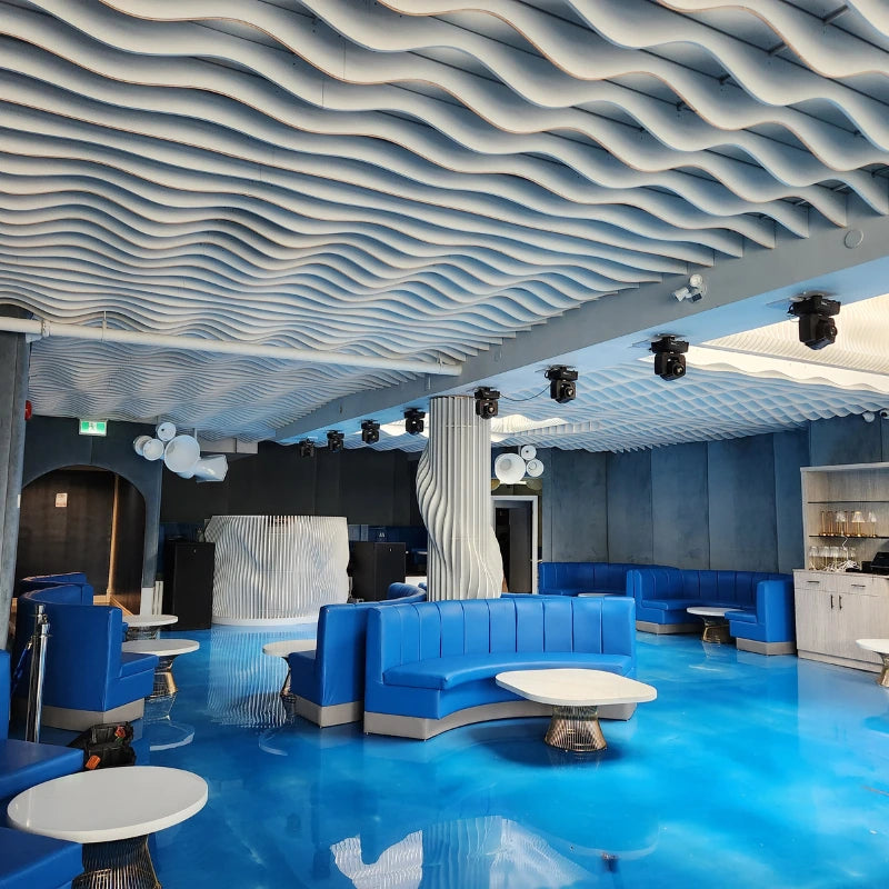 Modern interior with blue sofas and tables against a wavy ceiling.